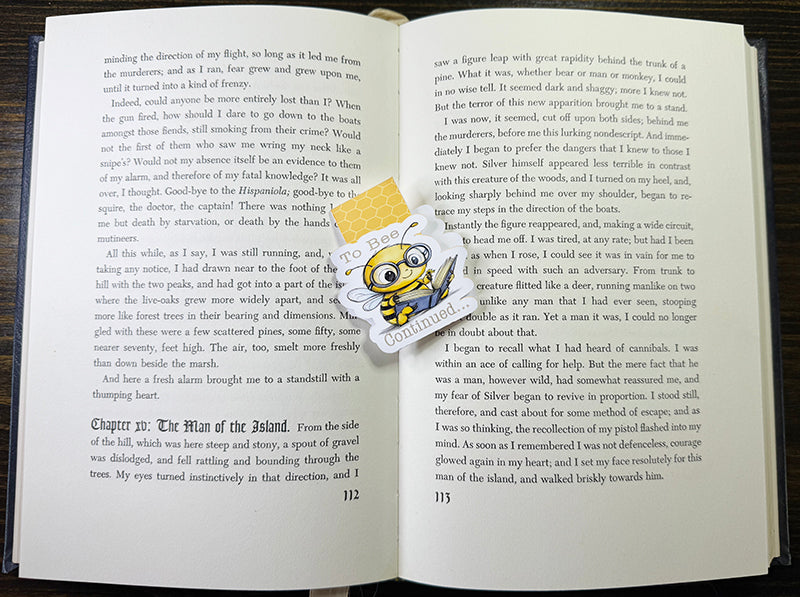 Cute magnetic bookmark with cartoon bee in glasses holding a book and the phrase “To Bee Continued…”