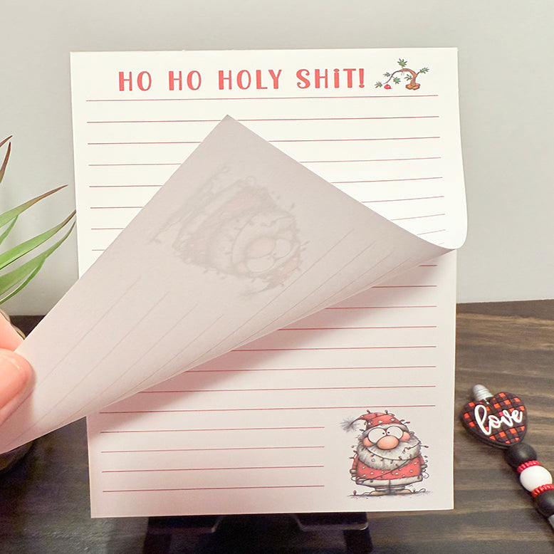 Funny Christmas 5x7 notepad with “Ho Ho Holy Shit!” in red text, lined pages, and a Santa illustration—shown with a page being flipped to show tear off page design.