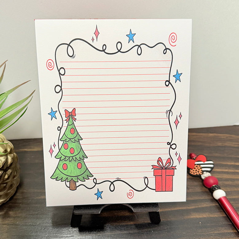 5x7 Christmas notepad with a decorated tree, wrapped gift, and festive red lines surrounded by string lights and stars – holiday stationery for notes and lists.