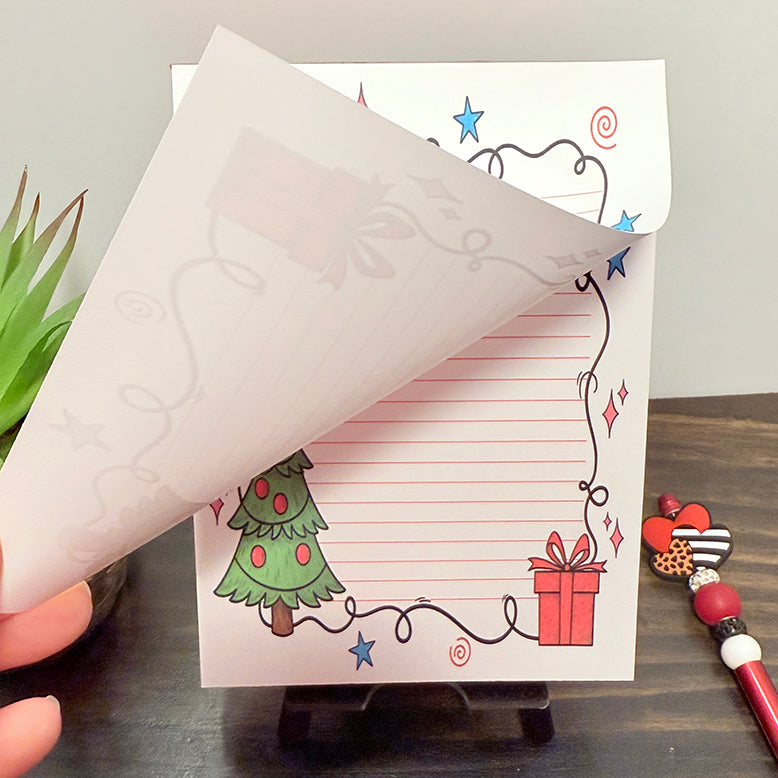 Christmas 5x7 notepad with festive red lines, decorated tree, and wrapped gift design – showing a page being lifted to reveal the tear off pages.