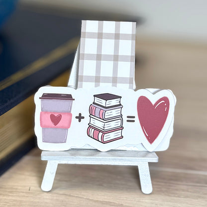“Close-up of coffee and books magnetic bookmark with illustrated latte, book stack, and heart, attached to neutral plaid magnetic tab.”