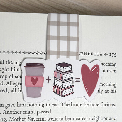“Magnetic bookmark with coffee cup, book stack, and heart design clipped to the top of a page, showing neutral plaid tab.”