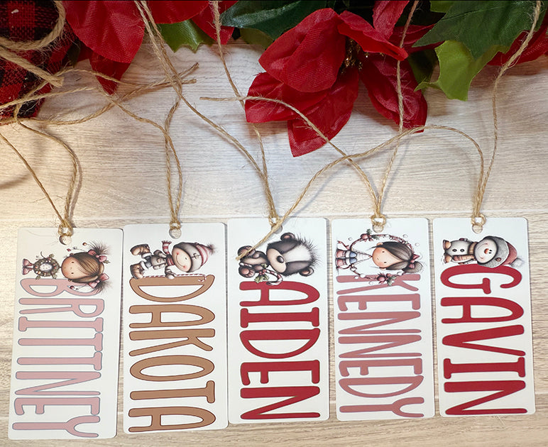 Flat lay of multiple personalized Christmas bag tags with names like Brittney, Dakota, Aiden, Kennedy, and Gavin, each featuring adorable holiday character designs.