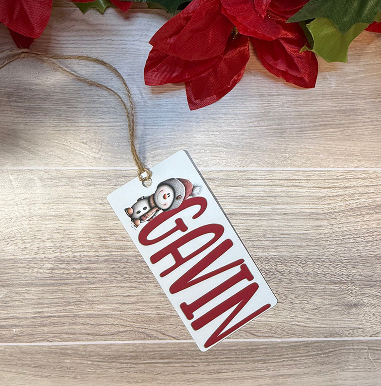 Flat lay of a personalized Christmas bag tag with the name Gavin and a cheerful snowman character wearing a Santa hat.