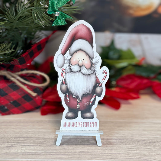 “Santa classic bookmark standing on a small easel, featuring a cute Santa holding candy canes with the phrase ‘Ho Ho Holding Your Spot!’ at the bottom.”