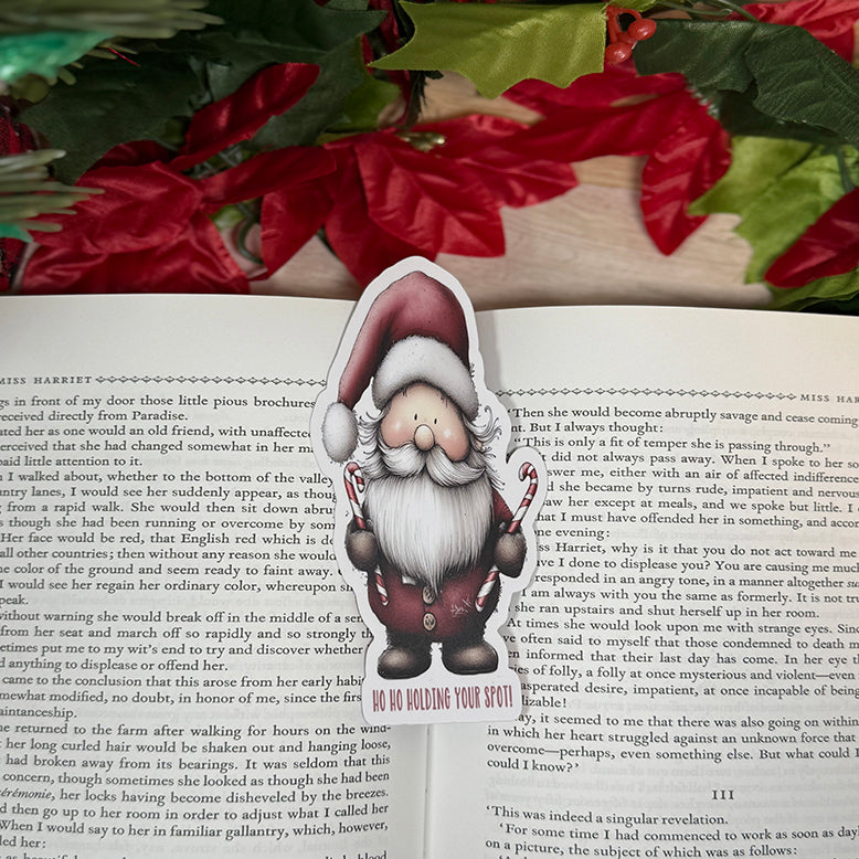 “Santa classic bookmark standing on a small easel, featuring a cute Santa holding candy canes with the phrase ‘Ho Ho Holding Your Spot!’ at the bottom.”