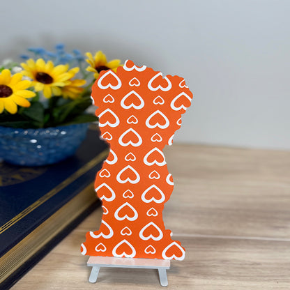 “Back of teddy bear classic bookmark featuring bold orange background with repeating white heart pattern, displayed upright on small stand.”