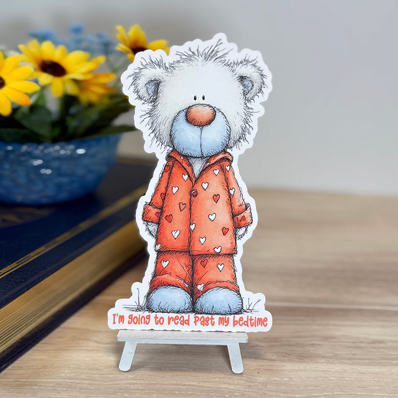 “Teddy bear classic bookmark standing on a small easel, wearing heart-print pajamas with the phrase ‘I’m going to read past my bedtime’ at the bottom.”