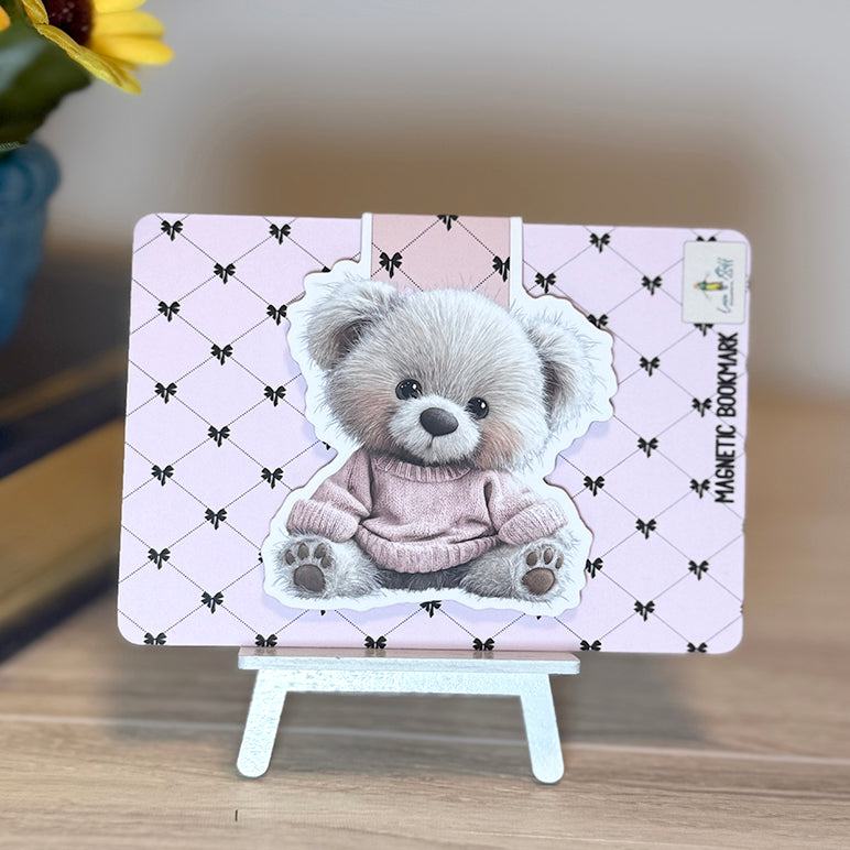 “Teddy bear magnetic bookmark attached to pink backing card with black bow pattern, displayed on small stand.”