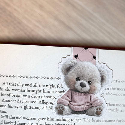 “Pink sweater teddy bear magnetic bookmark clipped to the top of a book page with pink bow-pattern tab visible.”