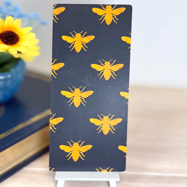“Back of bee-themed bookmark featuring repeating yellow bee pattern on a dark background.”