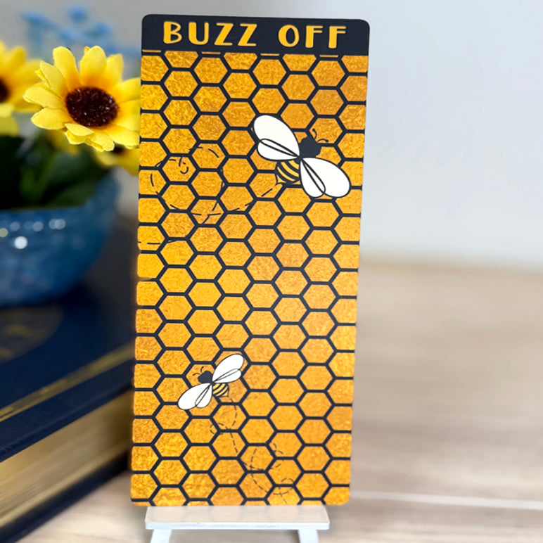 “Honeycomb bee-themed classic bookmark with ‘Buzz Off’ text displayed upright on a small stand with sunflower décor.”
