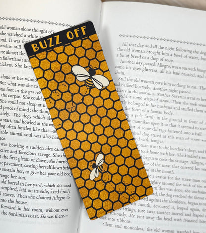 “Buzz Off honeycomb classic bookmark placed on the pages of an open book with bees and textured honeycomb design.”