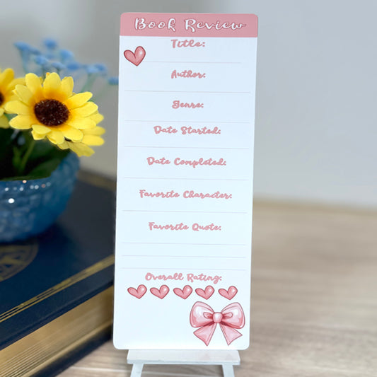“Book review bookmark standing upright with pink accents, heart icons, and lines for title, author, genre, dates, and rating.”