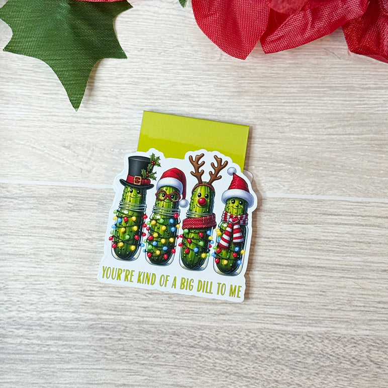 “Flat lay of Christmas pickle magnetic bookmark with four cute pickles wearing Santa hats and reindeer antlers.”