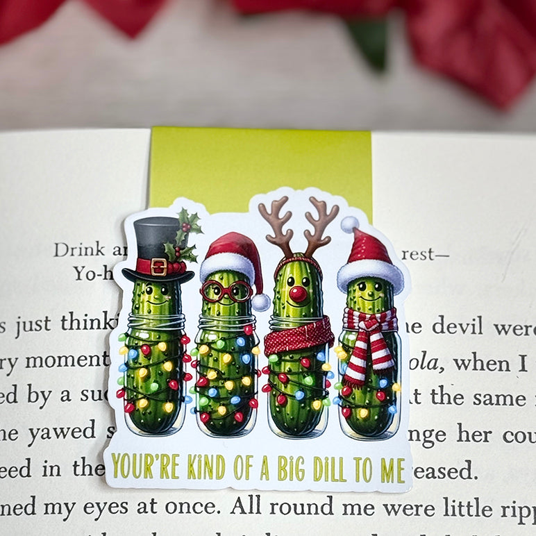 “Christmas pickle magnetic bookmark on an open book featuring four festive pickles with holiday lights and hats.”
