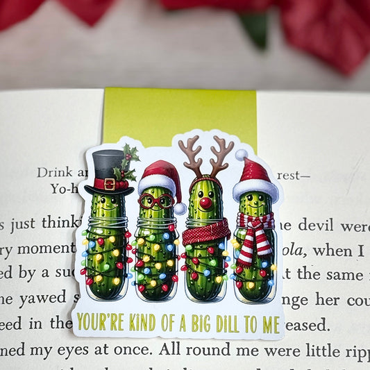 “Christmas pickle magnetic bookmark on an open book featuring four festive pickles with holiday lights and hats.”