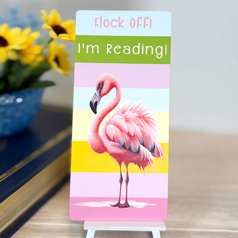 “Classic flamingo bookmark with the phrase ‘Flock Off I’m Reading’ displayed upright with pastel stripe background.”