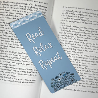 “Read Relax Repeat blue bookmark placed inside an open book showing floral illustration and heart border.”