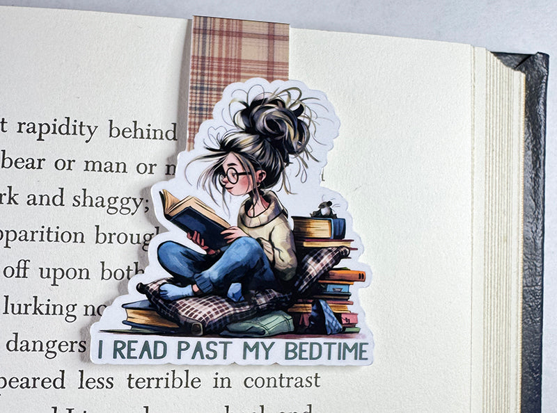 Magnetic bookmark with girl reading past bedtime, surrounded by books and pillows, with plaid tab
