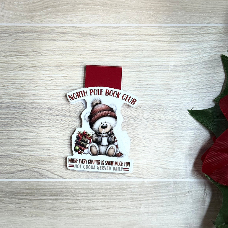 “Flat lay of North Pole Book Club magnetic bookmark featuring a bear in a winter hat holding hot cocoa.”
